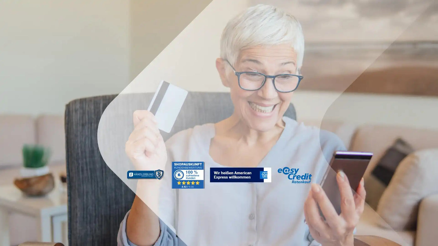 Eine lächelnde ältere Frau, die eine Kreditkarte und ein Smartphone hält.