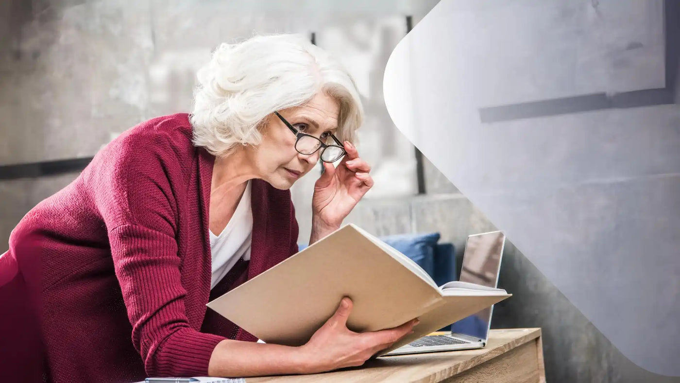 Eine ältere Frau in einem roten Cardigan und mit Brille liest ein Buch.
