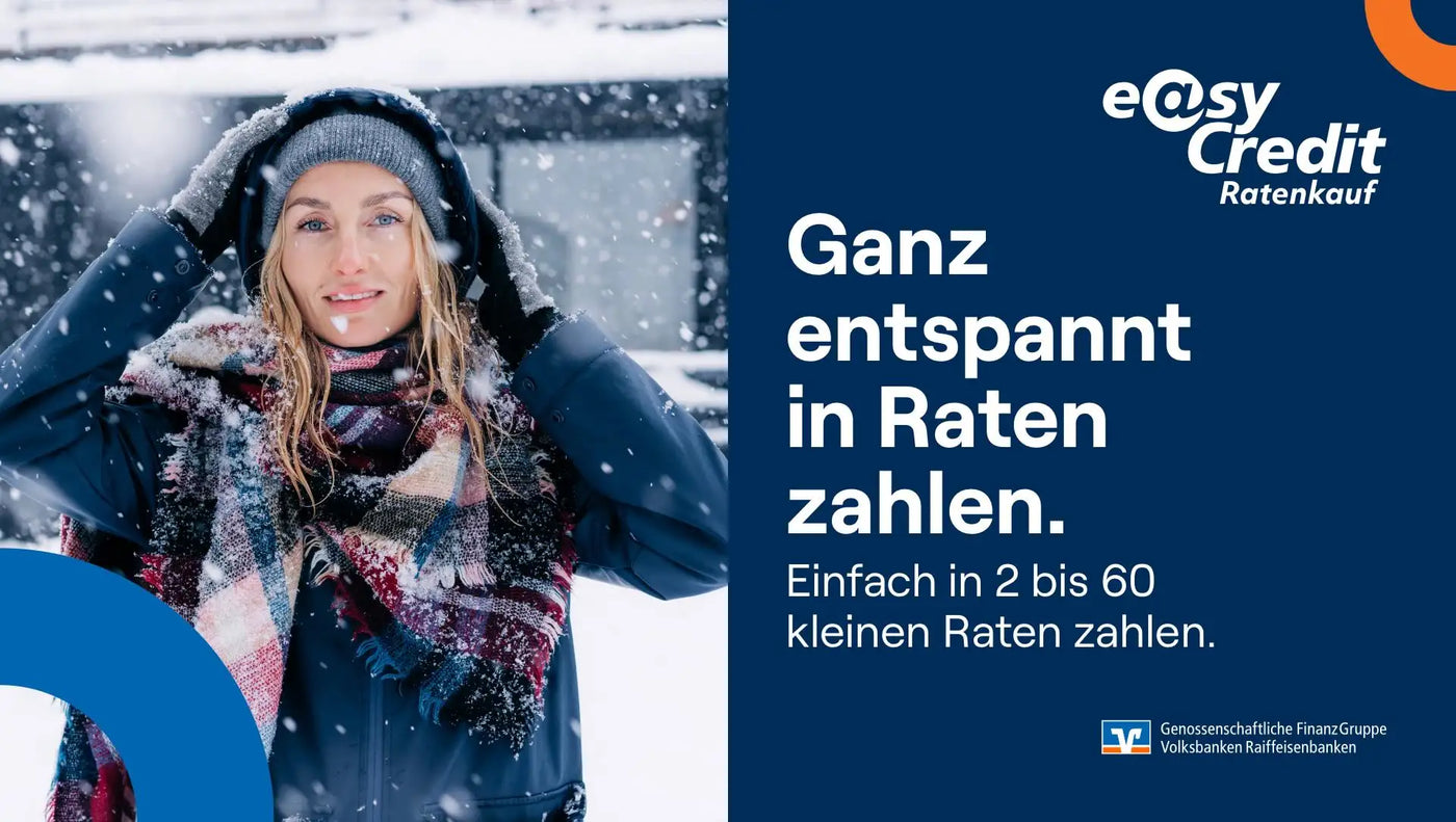 Eine Frau, die eine graue Strickmütze, einen dunkelblauen Wintermantel mit Schnee darauf und einen farbenfrohen karierten Schal in Schattierungen von Rot, Lila und Beige trägt.